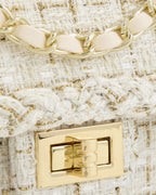 Close-up detail of polished gold turn-lock clasp and woven braided edge on cream tweed handbag