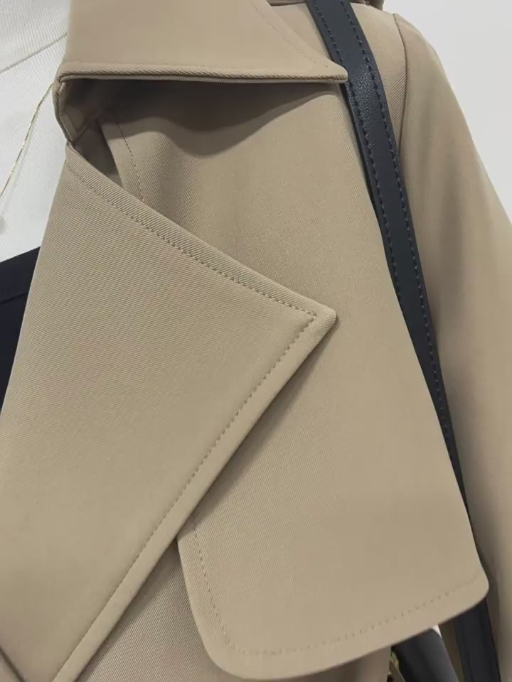 A close-up panning video that starts on the sharp stitching of the trench coat's lapels and slowly zooms out to reveal the full upper body. It highlights the fabric texture, the black button details, and the layered design of the storm flaps.
