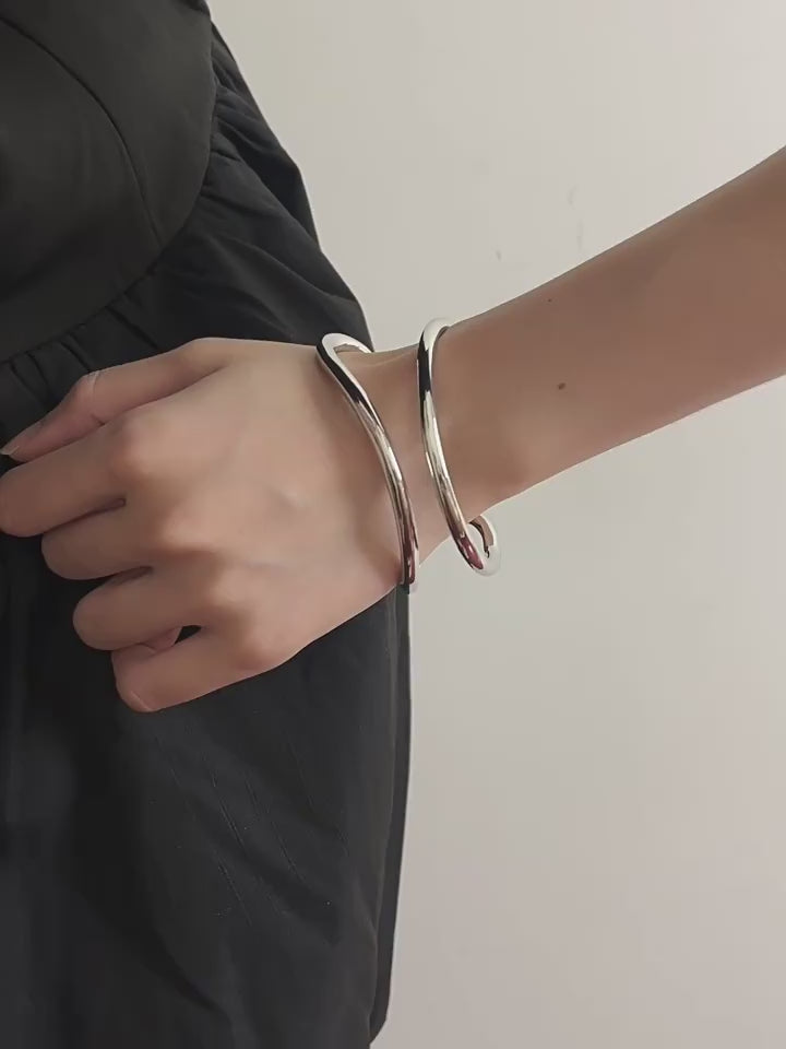 Video demonstration of the silver fluid wave bangle, showing how the light reflects off its polished, sculptural metal surface.