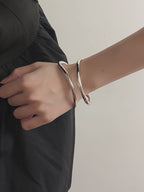 Video demonstration of the silver fluid wave bangle, showing how the light reflects off its polished, sculptural metal surface.